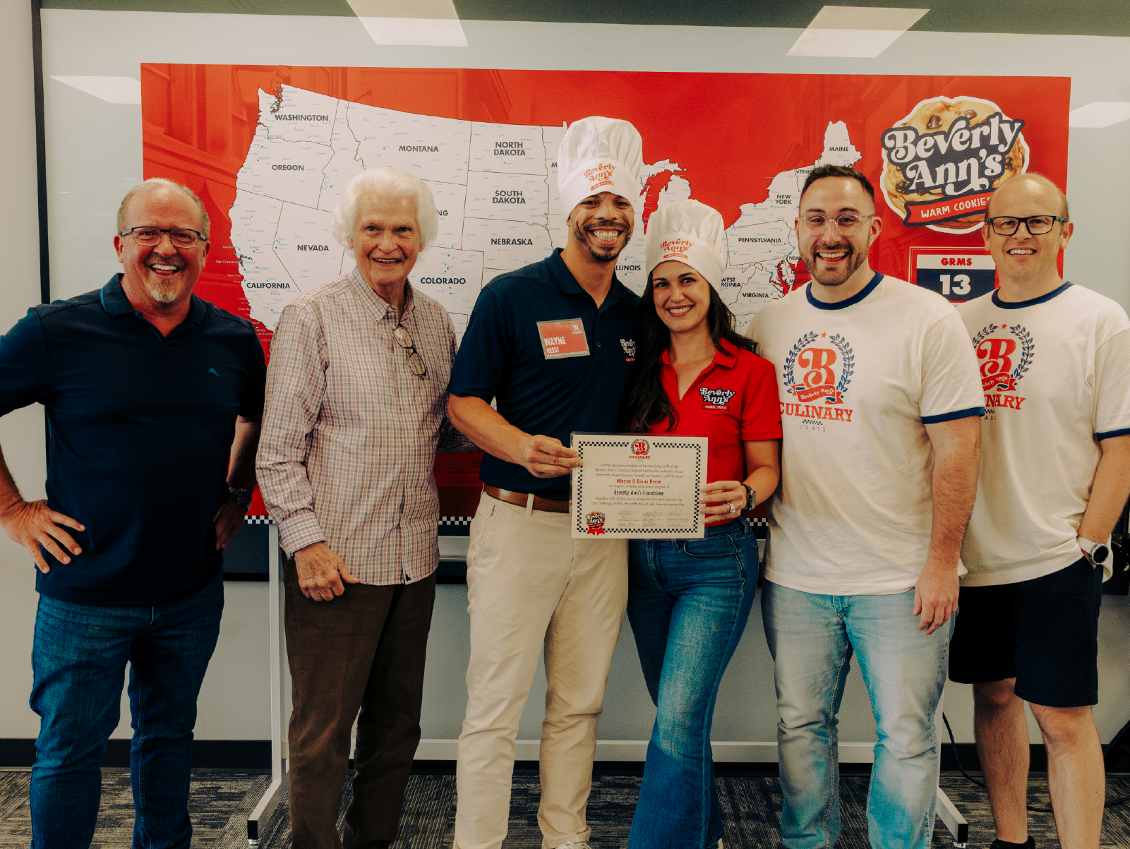 Travelin’ Tom’s team members standing with graduates of The Travelin' Tom’s Coffee Academy in front of a map of franchise locations