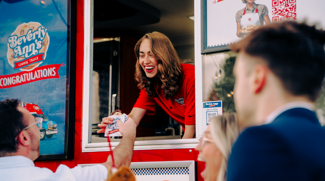  A Travelin’ Tom’s owner stands in her coffee truck and smiles while throwing her arms up in celebration